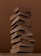 Broken dark chocolate bars stack isolated on block background