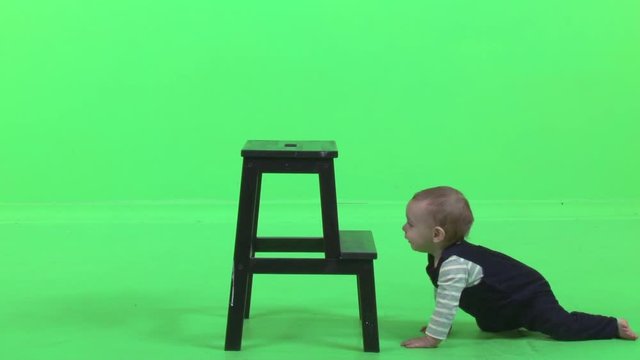 A cute little baby boy laughs happily while he stands over a green screen.