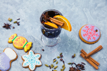 Mulled wine in glass mug with spices, female hands in knitted mittens.