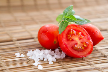 Fresh ripe cherry tomato, sea salt and a small branch of sweet basil on wooden background