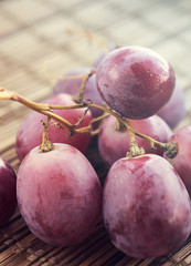 A small branch of red grapes on a rustic wooden surface lit by warm light.