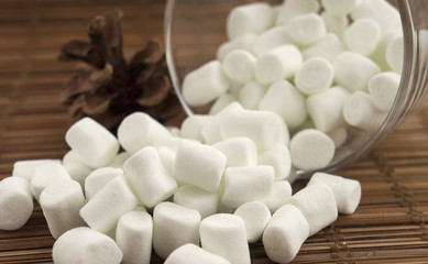 Fototapeta na wymiar Heap of white mini marshmallows, pine cone, wooden table. Ingredients for autumn warm soft drinks