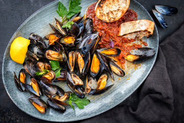 Traditional barbecue Italian blue mussel in tomato sauce with parsley and garlic in red wine sauce as top view on modern design plate