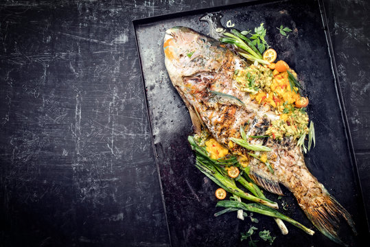 Traditioneller BBQ Papageienfisch mit Mango Salsa als Draufsicht auf einem schwarzen Board mit Textfreiraum links