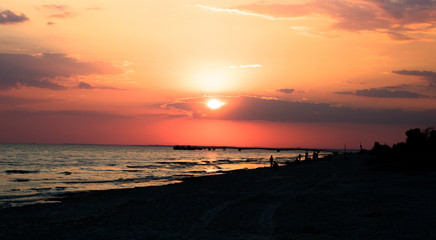Red sunset on the beach. People silhouettes and gull on the beach. Pier on the skyline