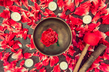 Top view tibetan singing bowl with floating inside in water red peony flower. Burning candles and...