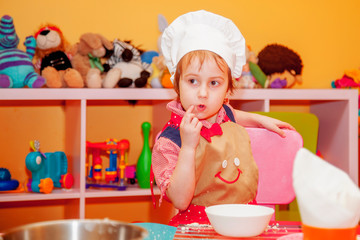 Beautiful little girl learns to cook a meal in the kitchen. Humorous photo.
