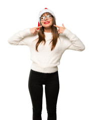 Obraz na płótnie Canvas Girl with celebrating the christmas holidays smiling with a pleasant expression while pointing mouth with fingers on isolated white background