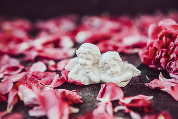 Statuette of two antique little lovely angels of the gypsum on the black stone background with pink...