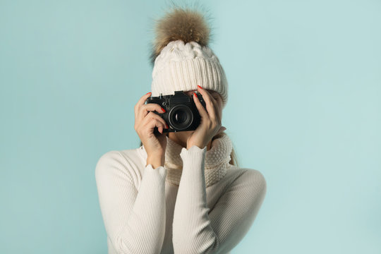 beautiful young girl in winter hat with a camera in hand on a blue background