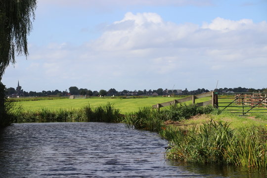 Water in a ditch around a meadow in Alphen aan den rijn with sun and blue sky with clouds