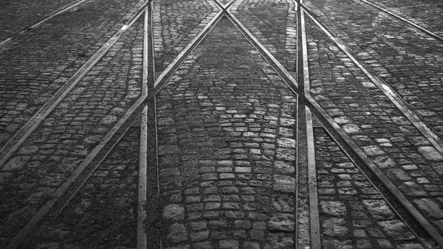 Crossing of tram rails on stone pavement in the city black and white background