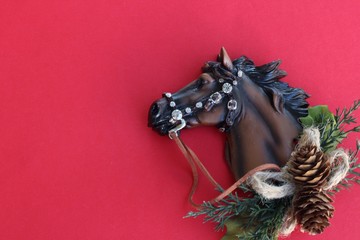 resin horse wearing bridle and reigns laying flat with pine cones and pine branches on a red background with writing space