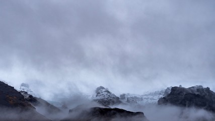 The snowy peaks of mountains revealed from behind the clouds on a winters day in Iceland