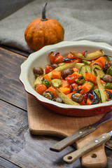 Rural still life of grilled vegetables and in a large ceramic plate and appliances on a wooden background. Copy space.