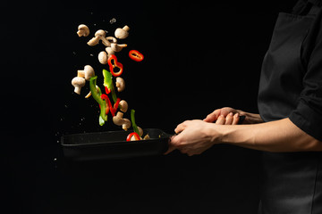 Professional cook. The chef prepares a dish with vegetables and mushrooms in a saucepan. on a black background. menu, recipe book, healthy food, restaurant business