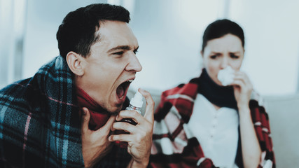 Sick Couple Sitting on Sofa in Checkered Blankets.