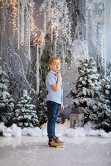 Christmas portrait of happy child boy with big glasses holding toy bear indoor studio, snowy winter decorated tree in blue colors on background. New Year Holidays