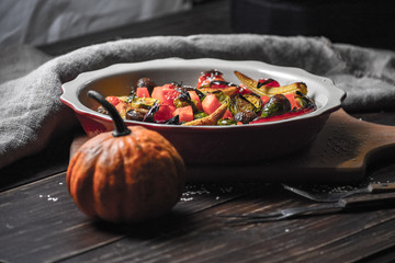 Rural still life of grilled vegetables and in a large ceramic plate and appliances on a wooden background. Copy space.