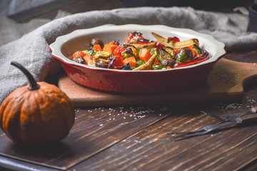 Rural still life of grilled vegetables and in a large ceramic plate and appliances on a wooden background. Copy space.