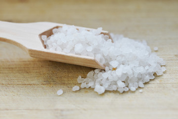 Granulated sea salt in wooden spoon, natural mineral isolated on the brown background