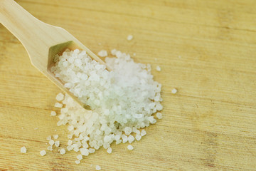 Granulated salt in wooden spoon prepared for beauty treatment at spa, natural mineral isolated on the brown background
