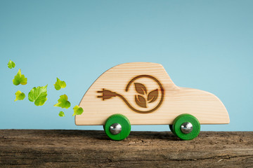 Concept of eco car. Wooden toy car with leaves and electric plug symbols impressed on the side.