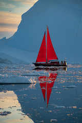 Greenland midnight Sunset iceberg calm mirror ocean with red sail ship reflected 