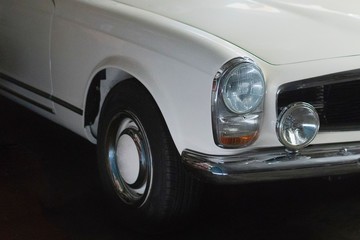 Obraz na płótnie Canvas Weißer Oldtimer Sportwagen steht in einer großen Garage Tuch zum Abdecken hängt in die Windschutzscheibe