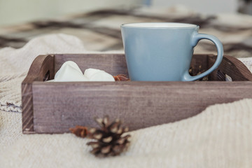 Cup of coffee on rustic wooden tray, sweet marshmallow and warm woolen sweater. Cozy autumn or winter weekend or holidays at home. Fall home decoration with hot drink mug. Hygge morning style concept