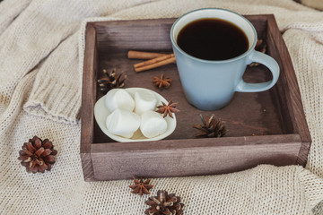 Cup of coffee on rustic wooden tray, sweet marshmallow and warm woolen sweater. Cozy autumn or winter weekend or holidays at home. Fall home decoration with hot drink mug. Hygge morning style concept