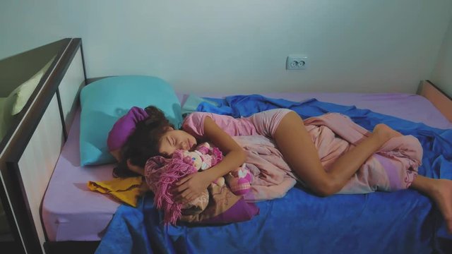Adorable little girl sleep in the sofa bed and hug her baby doll. little brunette girl sleeping at night in bed childhood sweetheart. children lifestyle sleep concept