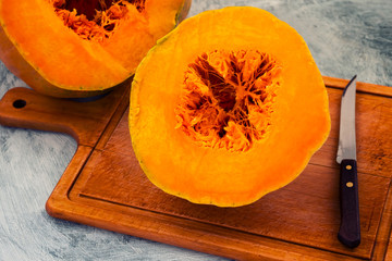 Ripe pumpkin with an orange middle, cut into two parts, a knife on a wooden Board.