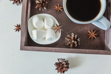 Cup of coffee on rustic wooden tray, sweet marshmallow and warm woolen sweater. Cozy autumn or winter weekend or holidays at home. Fall home decoration with hot drink mug. Hygge morning style concept