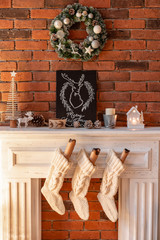 Fototapeta na wymiar White wool socks for Santa on the fireplace. Loft apartments, brick wall with candles and Christmas tree wreath.