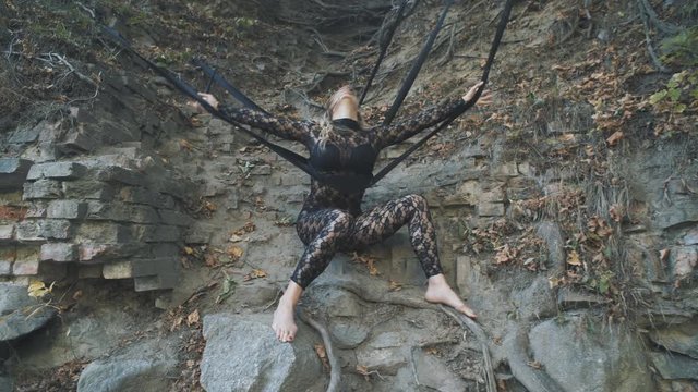 A beautiful blond girl in a body stocking tied with black ribbons to the roots is trying to free herself. Modern and fashion performance.