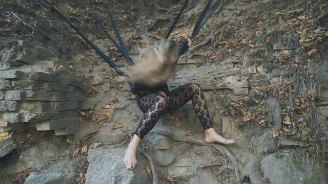 A beautiful blond girl in a body stocking tied with black ribbons to the roots is trying to free herself. Modern and fashion performance.