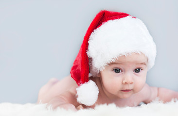 very beautiful bright emotional happy little baby in Santa hat crawling on white plaid