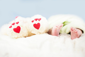 small tender legs of the baby, together with the paws of a Teddy bear with hearts on a white blanket
