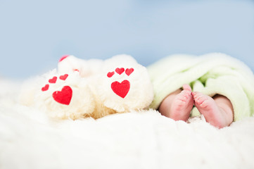 small tender legs of the baby, together with the paws of a Teddy bear with hearts on a white blanket