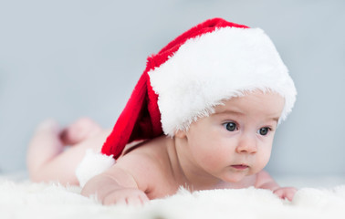 very beautiful bright emotional happy little baby in Santa hat crawling on white plaid