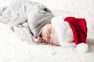 Obraz premium very beautiful bright happy little baby in Santa hat sleeping on white plaid wrapped in grey fabric on black background