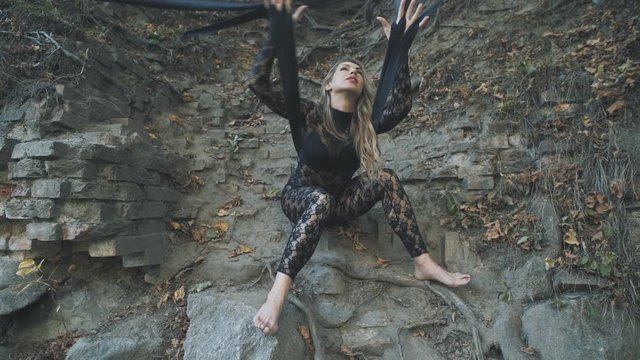 A beautiful blond girl in a body stocking tied with black ribbons to the roots is trying to free herself. Modern and fashion performance.