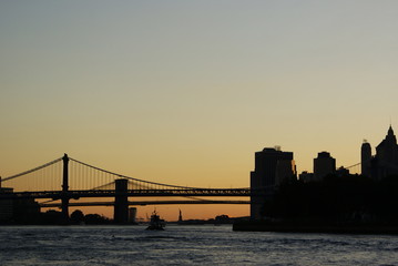 Silhouette of the Statue of Liberty and the Brooklyn Bridge at sunset.