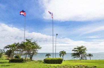 Thai flag and Cambodia flag on high pole under blue sky  at Thai - Cambodian borderline landmark number 73 marking pole indicating sign demarcation