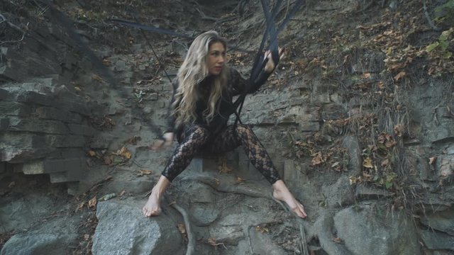 A beautiful blond girl in a body stocking tied with black ribbons to the roots is trying to free herself. Modern and fashion performance.
