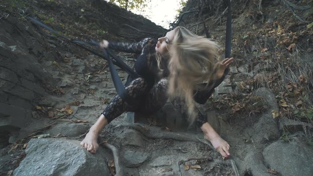 A beautiful blond girl in a body stocking tied with black ribbons to the roots is trying to free herself. Modern and fashion performance.