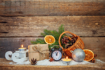 Christmas New Year composition winter objects gift box fir branch basket pine cones balls sled candle alarm clock on old shabby rustic wooden background. Xmas holiday december decoration copy space