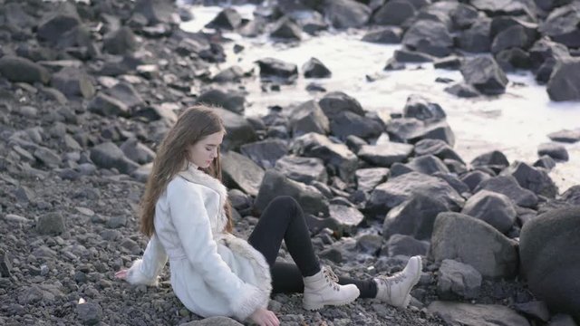 Cute girl sitting on the beach admiring the sunset and throwing pebbles into the sea 4k,30fps