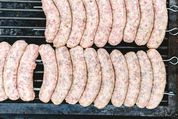 Many white sausages in a row to roast on a barbecue with charcoal.